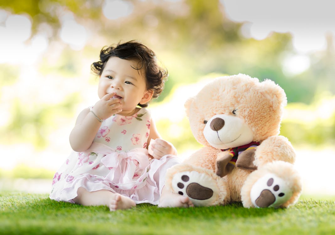 Free Baby Sitting on Green Grass Beside Bear Plush Toy at Daytime Stock Photo