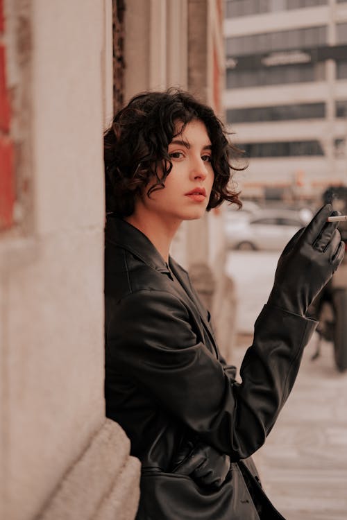 A Pretty Woman Leaning on Wall Holding a Lighted Cigarette