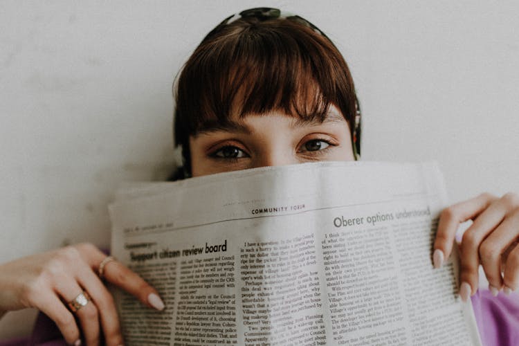 Young Woman Covering Half Of Face With Newspaper