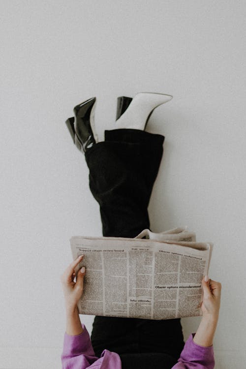 Free Woman in Fashionable Pants and Boots Sitting on Floor and Reading Newspaper Stock Photo