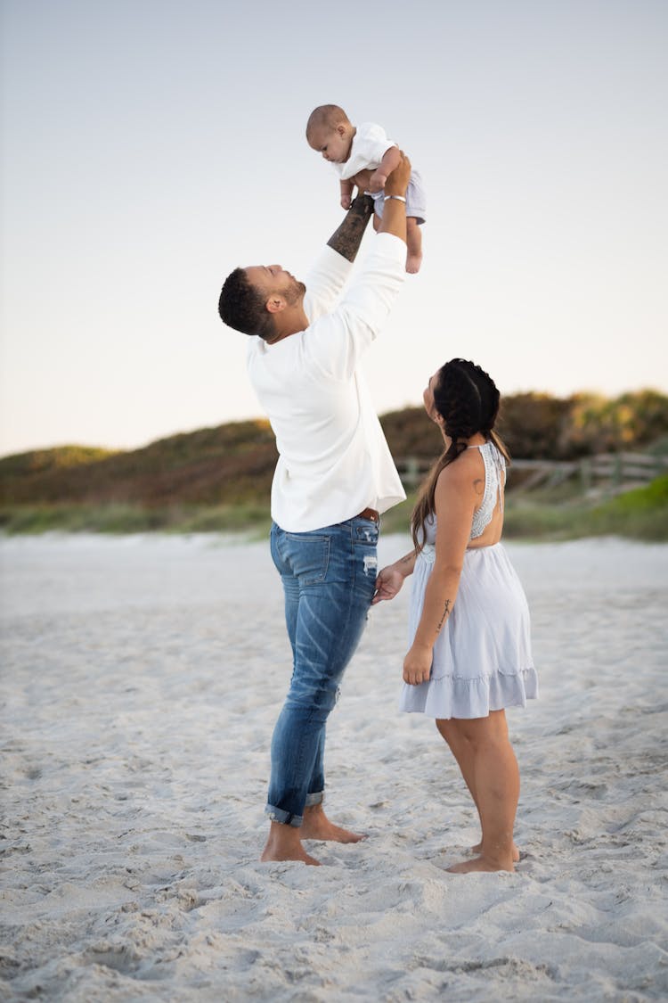 A Man Lifting His Baby While Standing Beside The Woman In Dress Looking Up