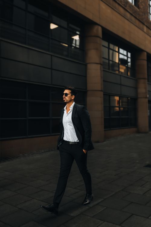 Free Man in a suit walking confidently with sunglasses in a city setting, showing style and business demeanor. Stock Photo