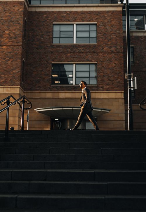 Free Side view of a businessman walking up stairs near a modern brick office building in daylight. Stock Photo