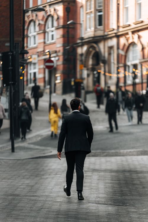 Free Man in a suit walking through a busy city street with historic architecture. Stock Photo
