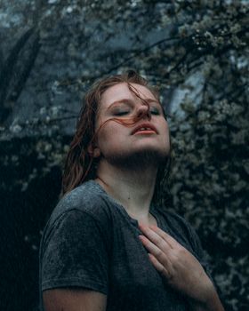 Portrait of a serene woman with closed eyes standing in the rain, embracing the natural elements.