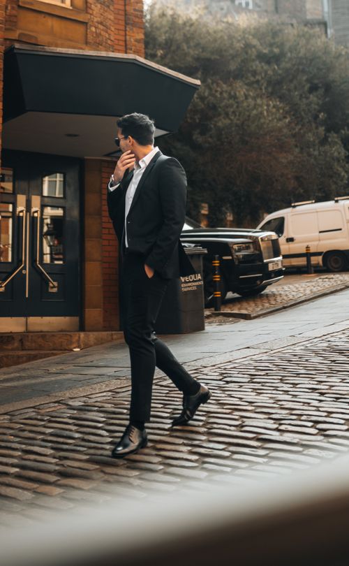 Free A fashionable man in a suit walks on a cobblestone street, exuding style and sophistication. Stock Photo
