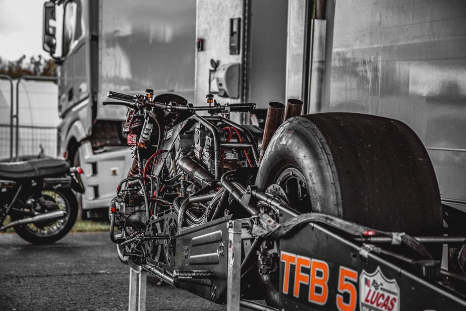 Close-up of a drag racing motorcycle with exposed engine in a paddock setting, ready for competition.