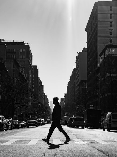 Free A silhouette of a man crossing a vibrant city street surrounded by tall buildings in black and white. Stock Photo