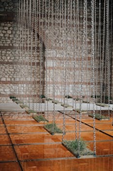 A modern art installation with chains and grass hanging from an indoor arch structure.