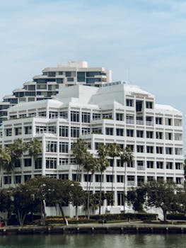 Contemporary white high-rise building by the water with palm trees.