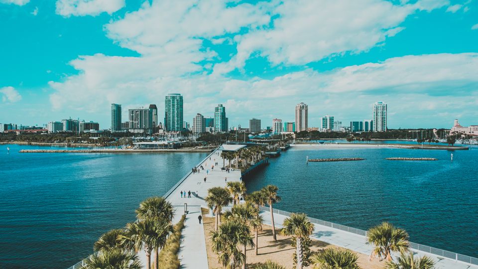 Enjoy a stunning aerial view of a Florida coastal city with palm trees, pier, and clear skies.