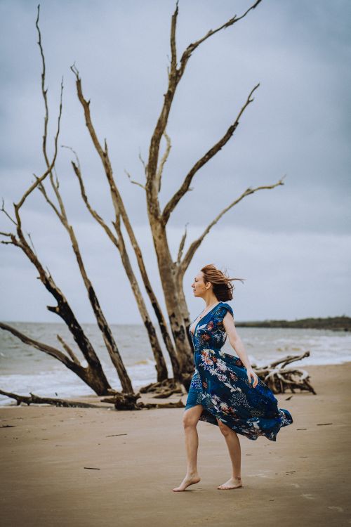 Free A woman in a floral dress poses gracefully on a windy beach in Jacksonville, FL. Stock Photo