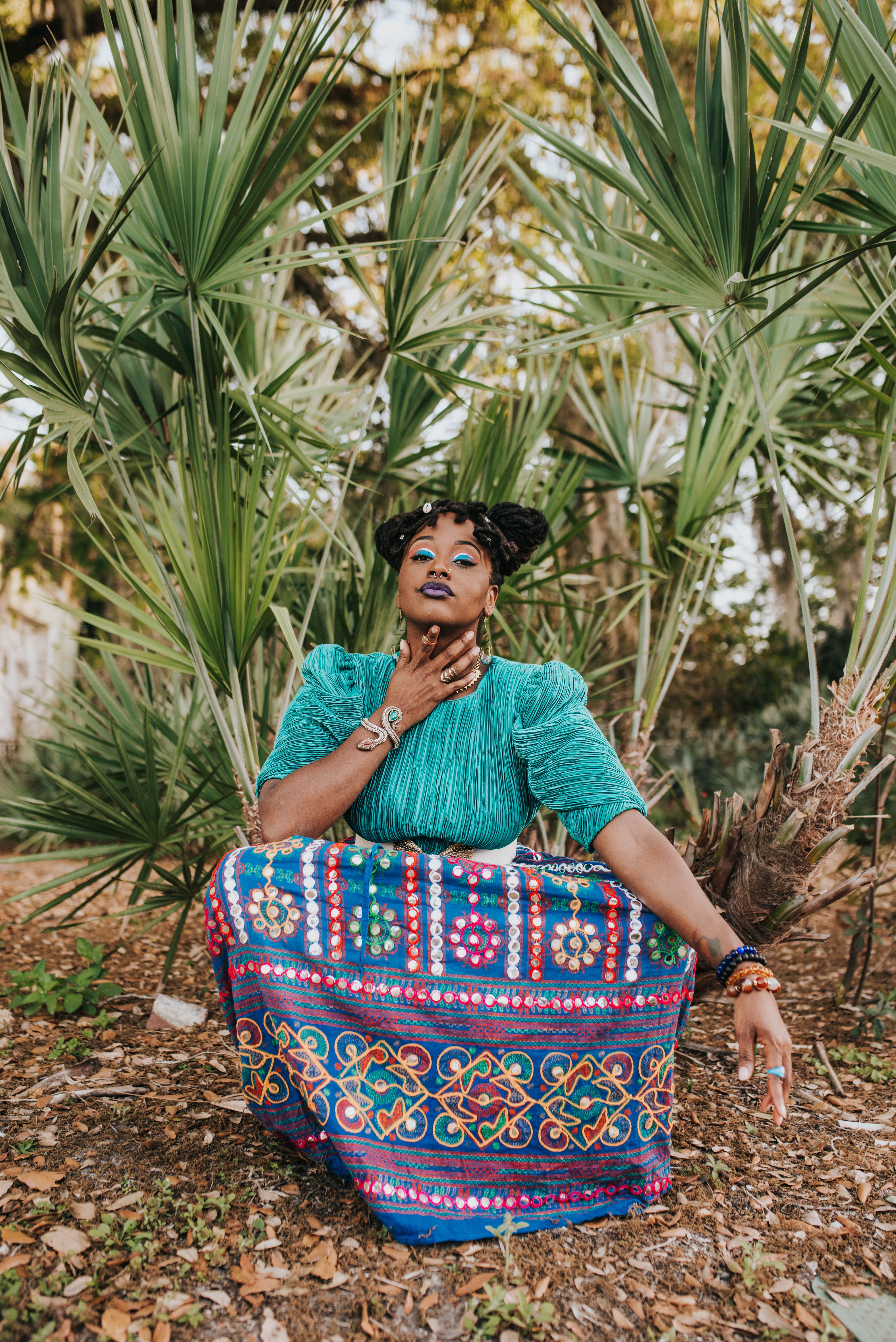 A striking portrait of a woman in vibrant, colorful clothing, surrounded by lush green plants.