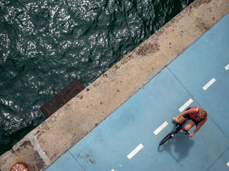 Aerial image of a woman cycling on a blue riverside path, showcasing a vibrant outdoor scene.