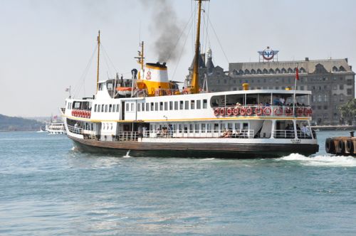 Free A traditional ferry sailing near a historic building in Türkiye, capturing a vibrant travel scene. Stock Photo