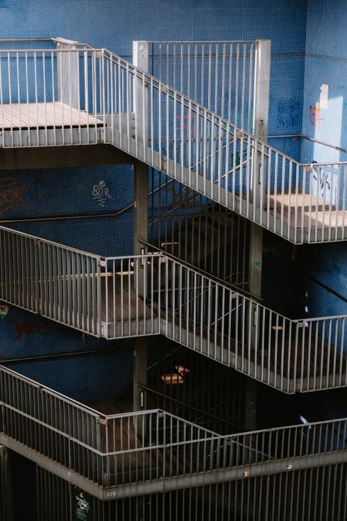 Free Vertical shot of industrial metal staircases with graffiti on a blue wall facade. Stock Photo