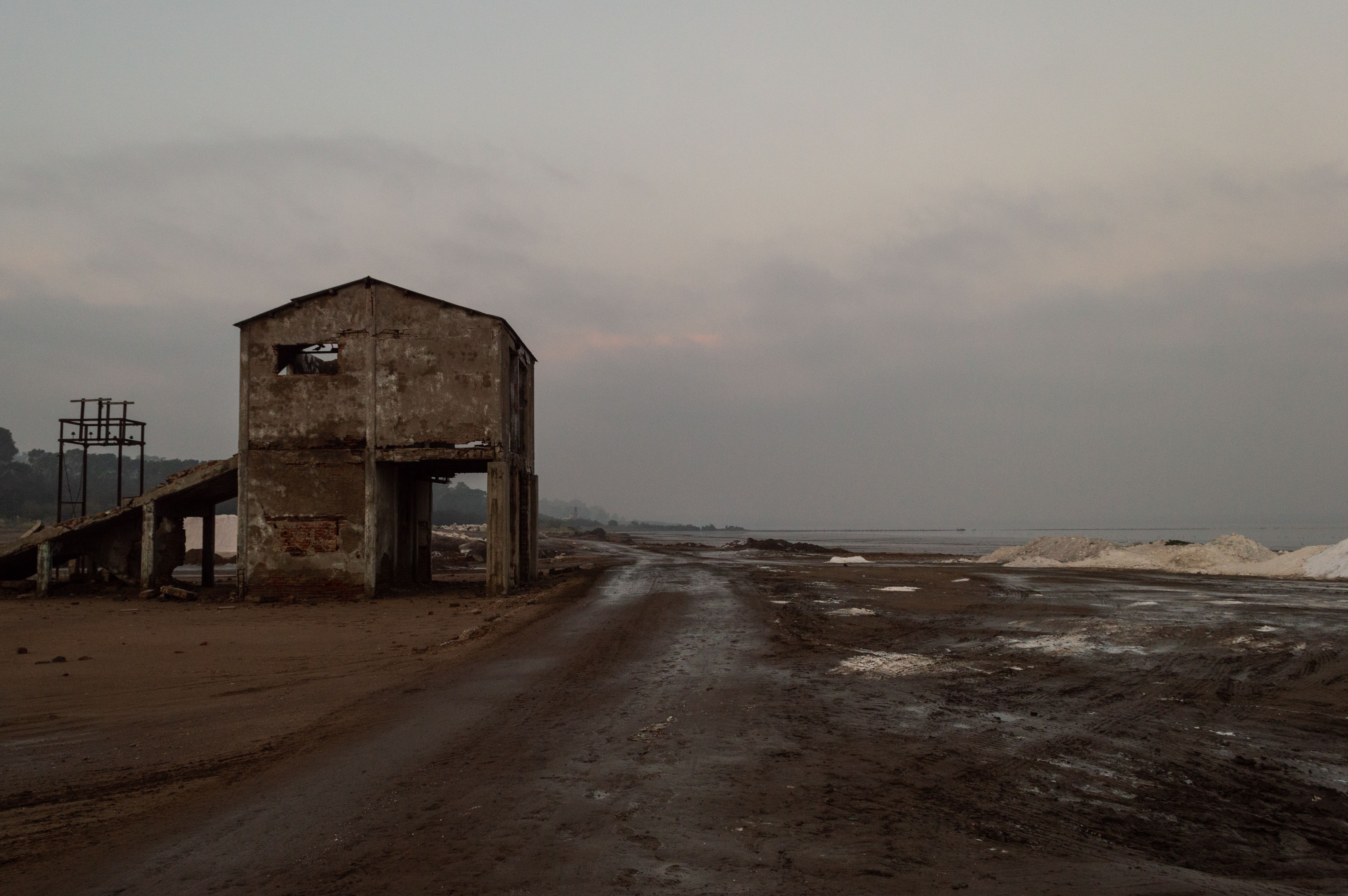 A solitary abandoned structure stands on a barren beach, evoking desolation at dusk.