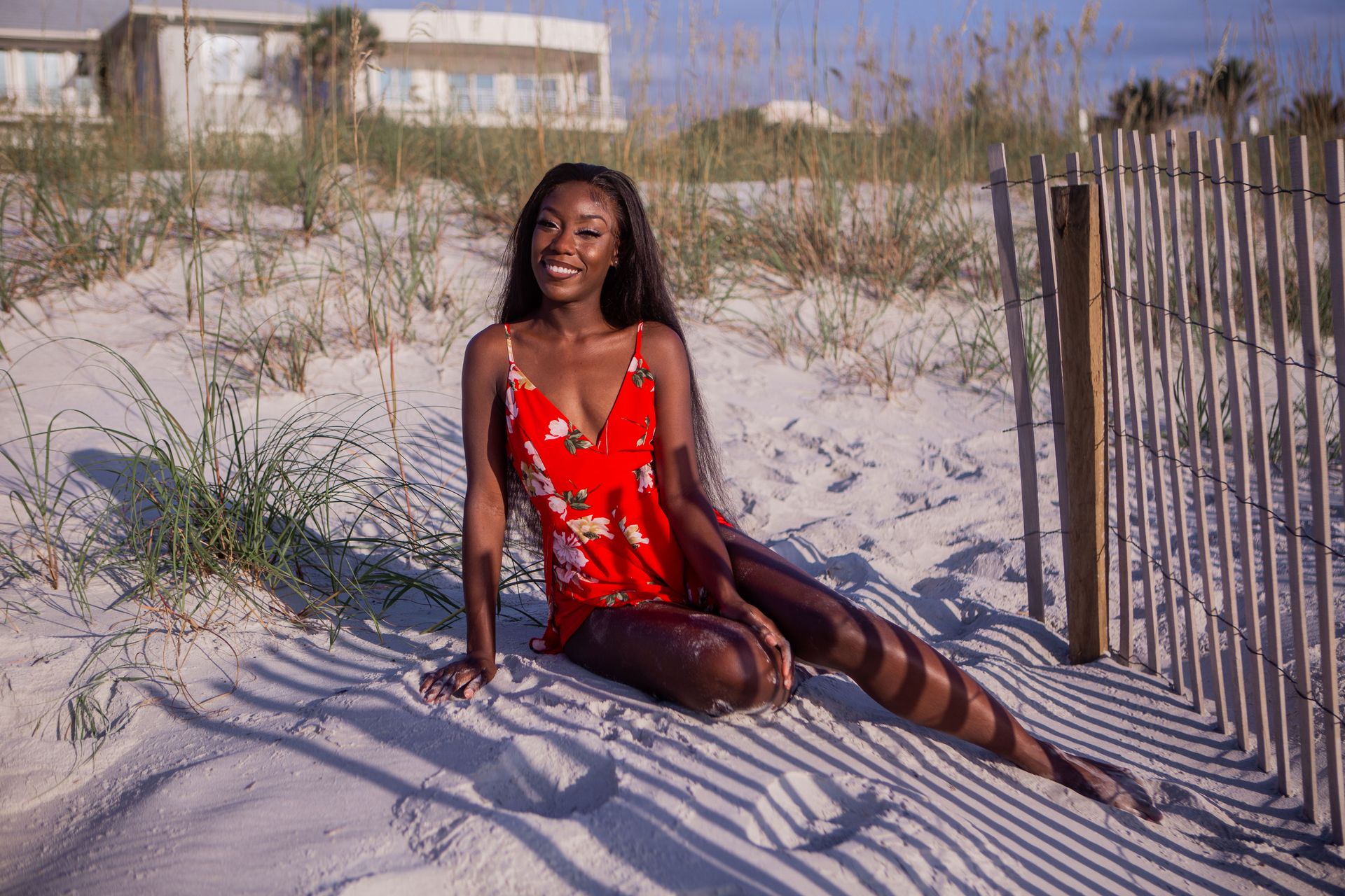 Smiling woman in a floral red dress enjoying the sun on a sandy Jacksonville beach.