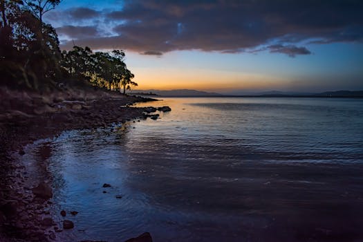 Peaceful shoreline of Lunawanna, Tasmania at twilight with calm waters and dramatic evening sky.