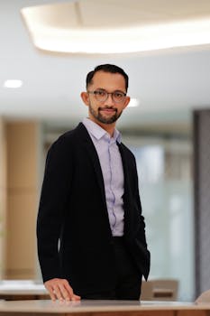Portrait of confident businessman with eyeglasses and blazer in modern office setting.