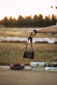 A vintage camera being held outdoors against a blurred sunset background, offering a nostalgic feel.