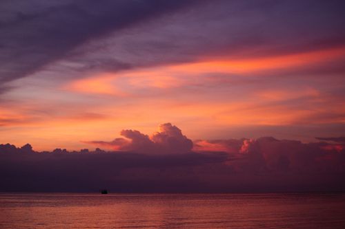 Free A breathtaking sunset with dramatic clouds and a distant silhouette over calm waters. Stock Photo