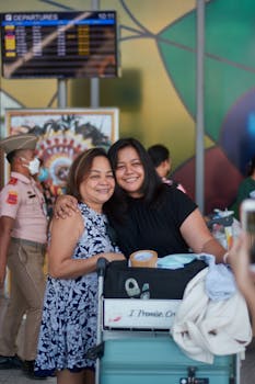 Smiling mother and daughter embrace at a busy airport terminal departure hall.