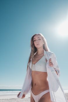 Striking low-angle shot of a woman in white bikini and shirt under clear blue sky.