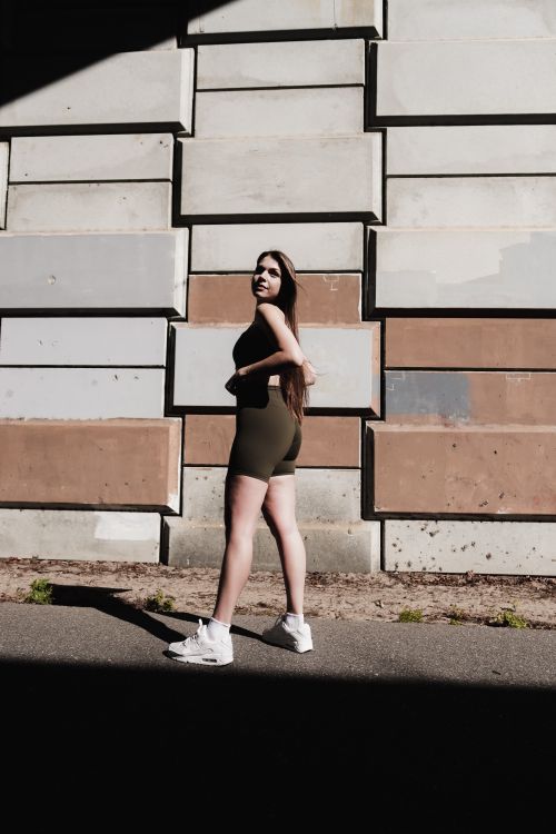 Free A woman in athletic wear posing confidently against a textured wall in an urban setting. Stock Photo