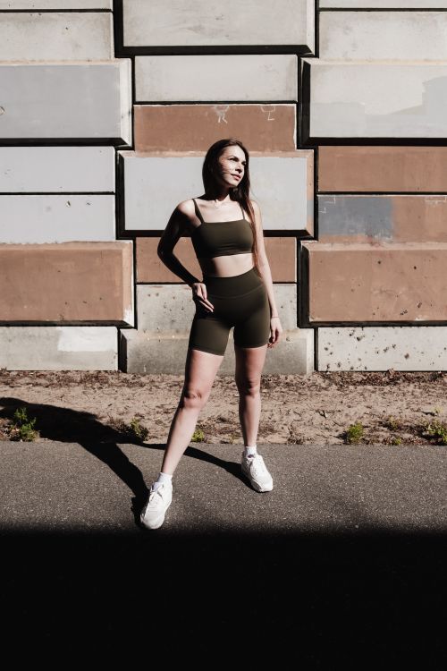 Free Confident woman in fashionable athletic wear posing against an industrial wall under sunlight. Stock Photo