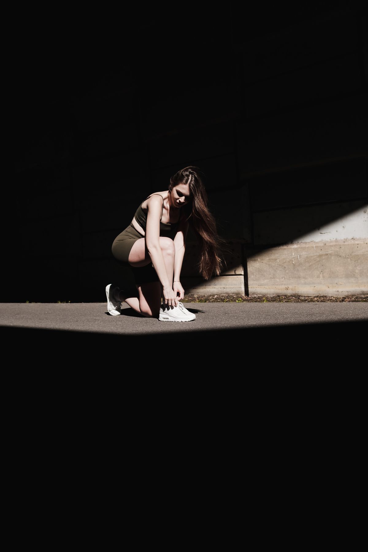 Woman in athletic wear sitting on concrete and tying her sneakers before a workout