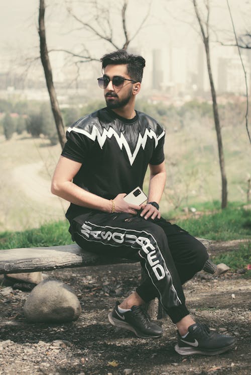 Free Man in Black and White Crew Neck T-shirt and Black Sunglasses Sitting on Brown Wooden Stock Photo