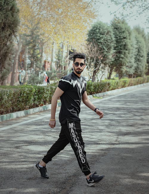 A Man in Black T-shirt and Black Pants Walking on the Street