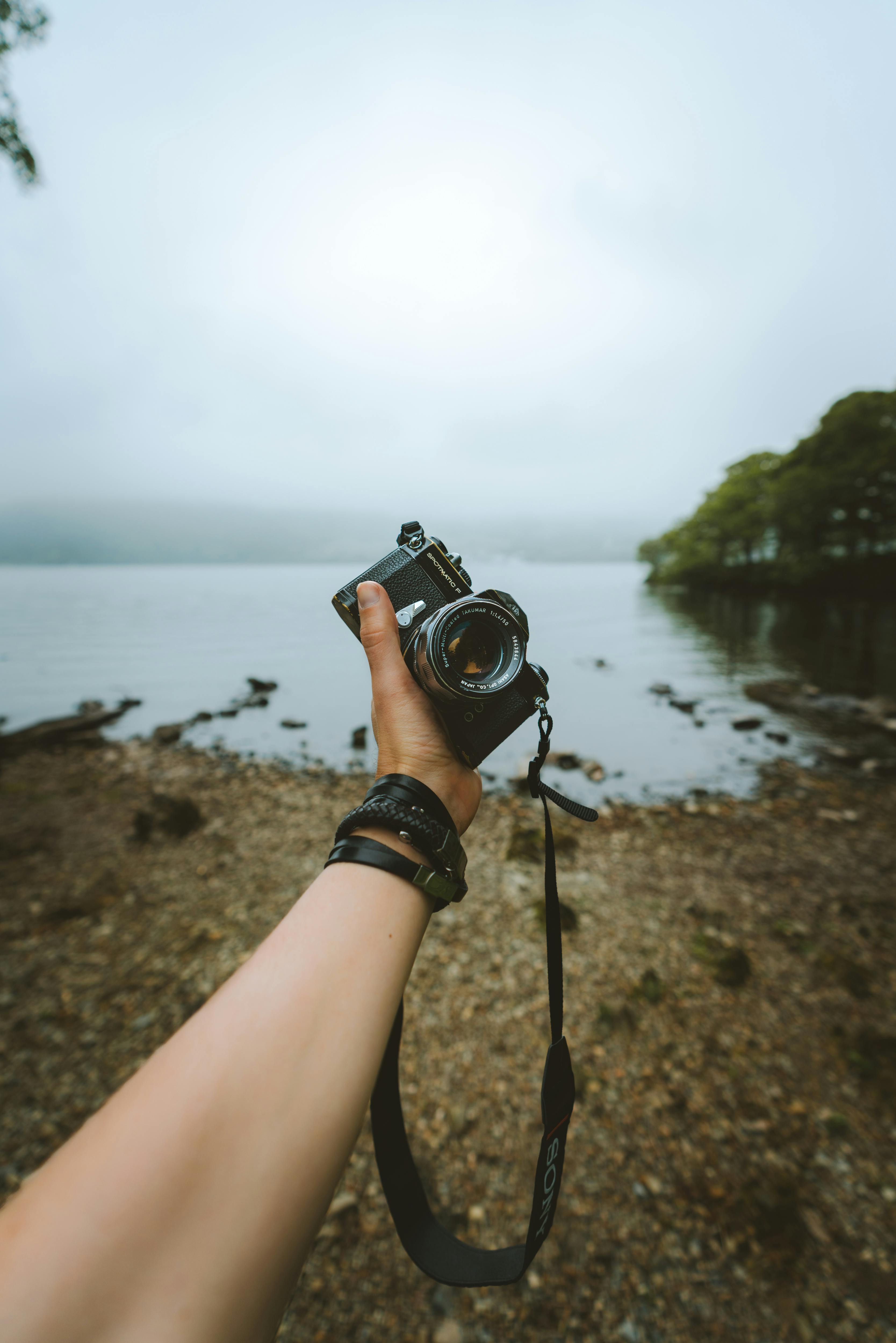 Person Holding Black Camera Front Body Of Water · Free Stock Photo