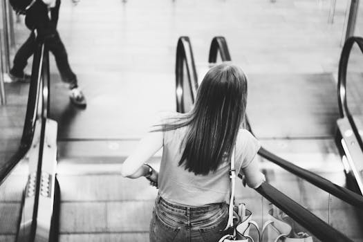 一张黑白照片中，一名女子站在自动扶梯上，背景是城市