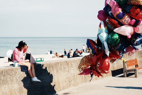 Woman Sitting on Gray Concrete Bench Next to Beach