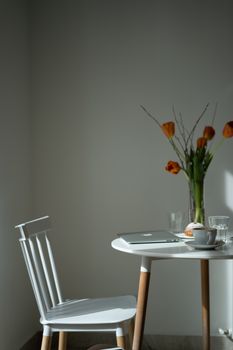 Cozy and minimalist workspace with a laptop, tulips, and a white chair by a sunny window.