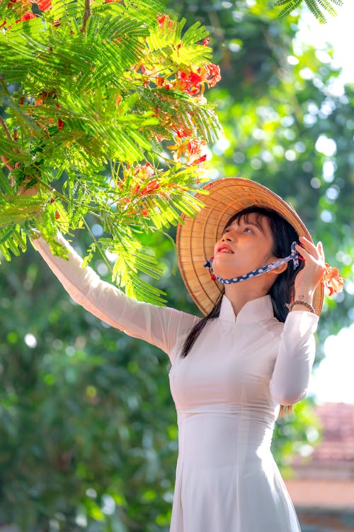 A Woman in Ao Dai Dress Wearing Rice Hat while Looking at the Green Plants
