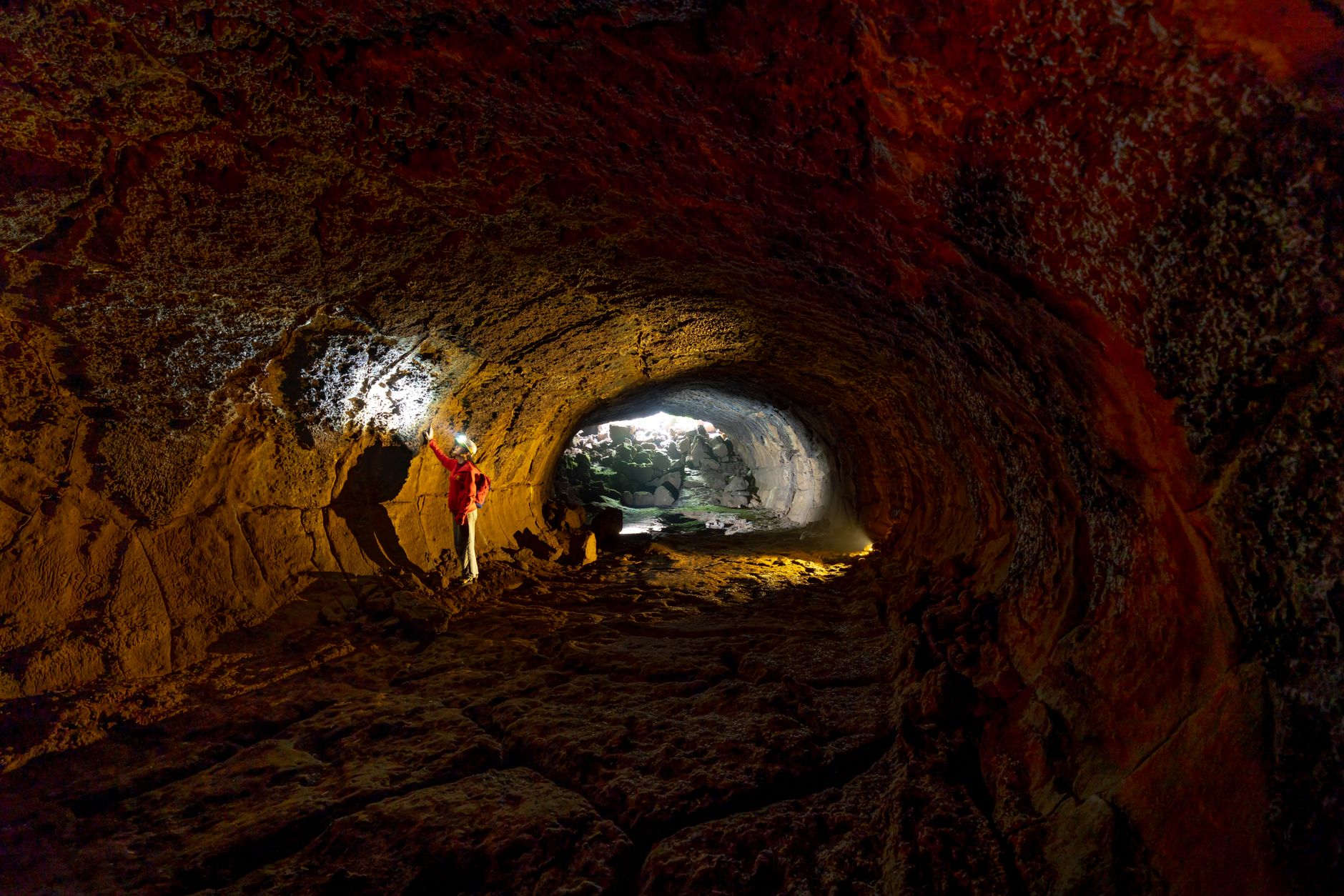 A person exploring a rugged cave with a flashlight, revealing textured walls.