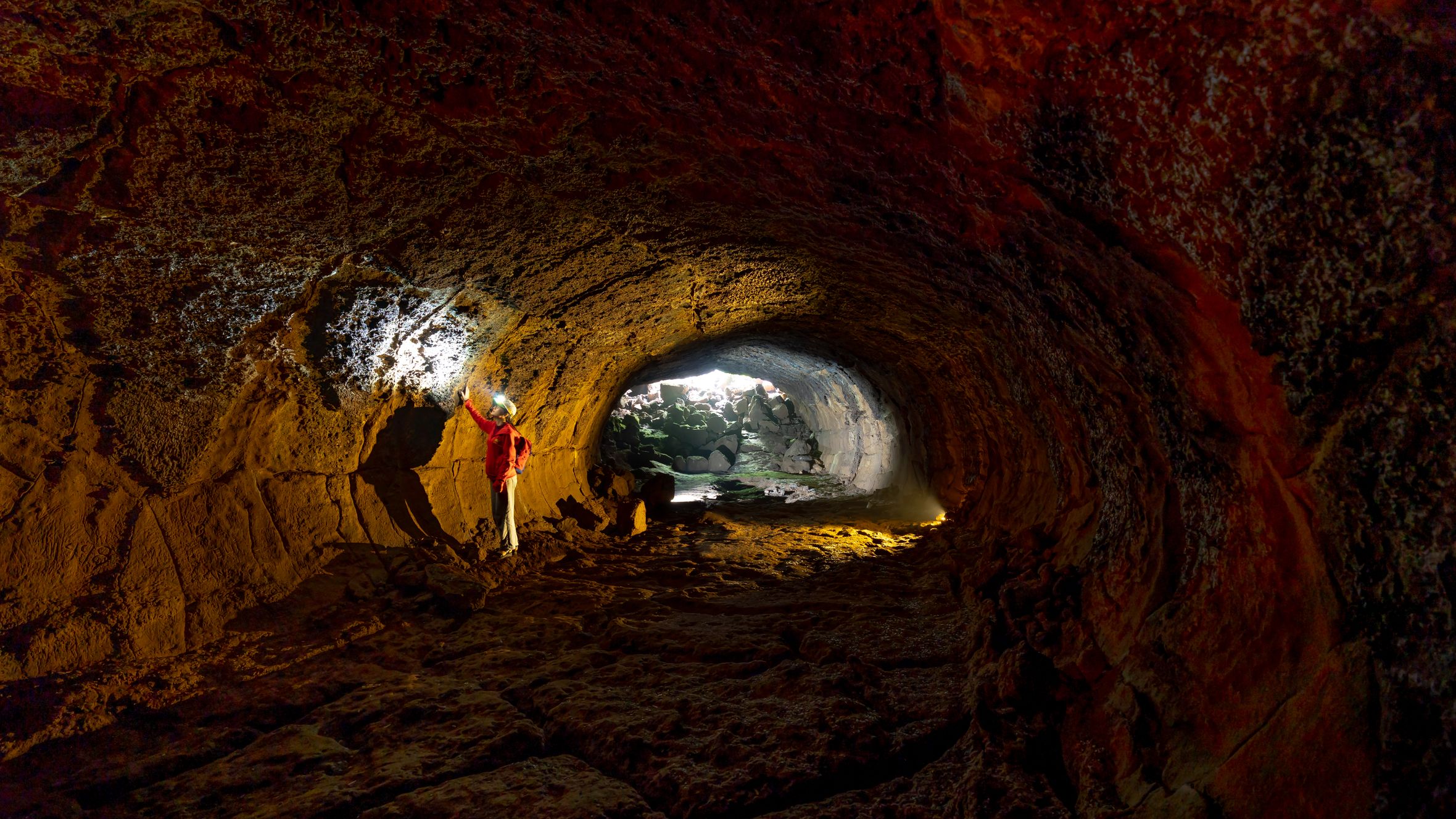 A person exploring a rugged cave with a flashlight, revealing textured walls.