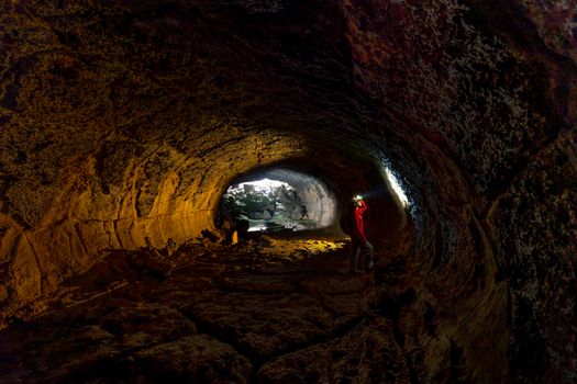 Man exploring a dark cave tunnel with light filtering through, showcasing natural stone formations.