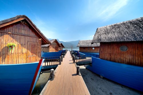 Free Charming wooden cabins with thatched roofs by a blue wooden pier under a clear sky. Stock Photo