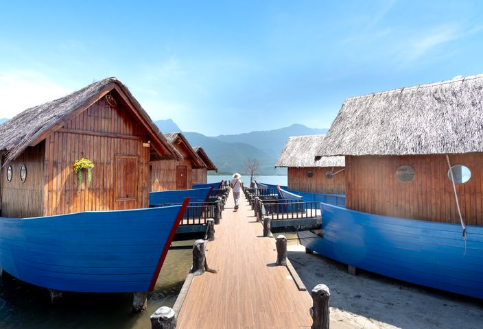 Wooden floating cabins on a serene boardwalk with mountain views, ideal for travel and relaxation.