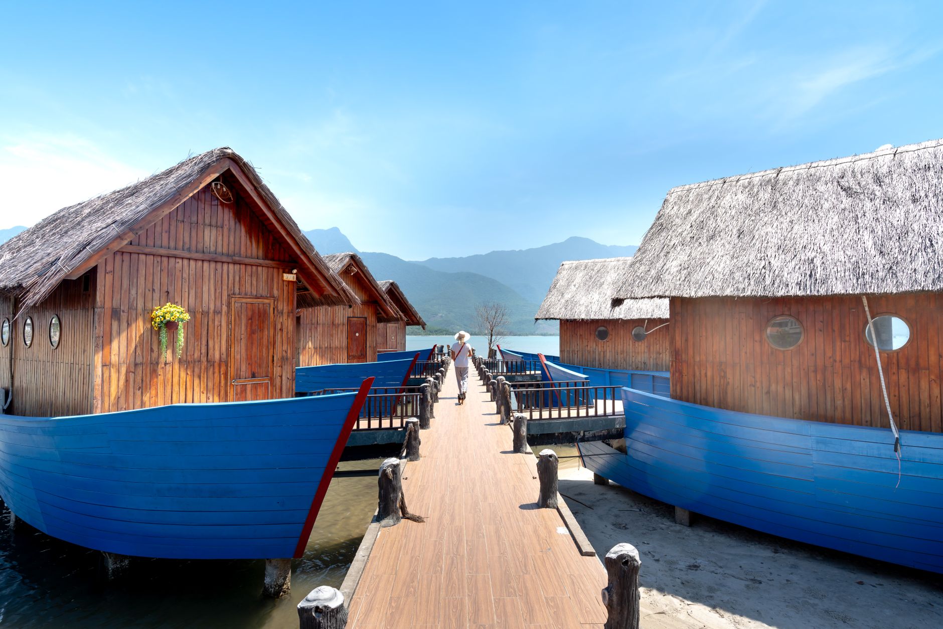 Wooden floating cabins on a serene boardwalk with mountain views, ideal for travel and relaxation.
