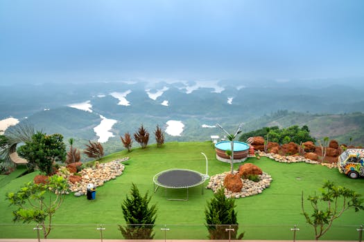 Beautiful garden with artificial grass, jacuzzi, and trampoline against mountains.