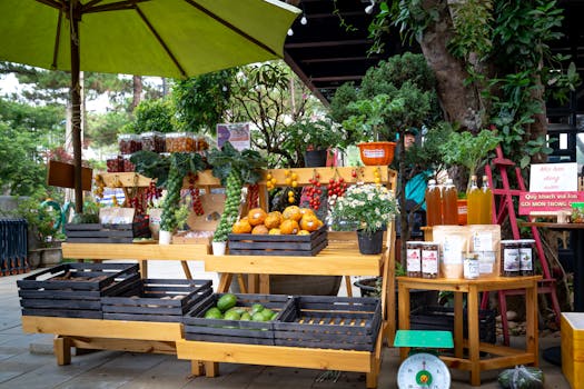 A colorful outdoor market stand showcasing fresh fruits, vegetables, and products under a green umbrella.