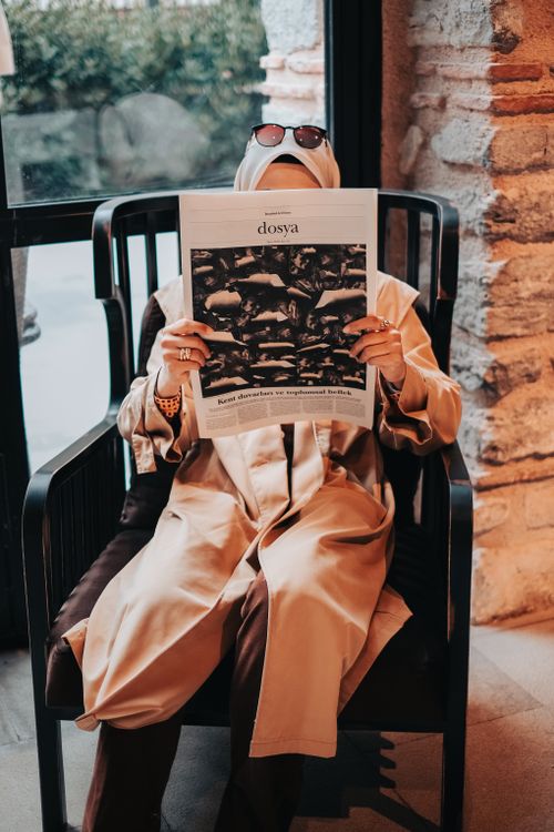 Free Woman in hijab reading a newspaper in a cozy café setting, seated and relaxed. Stock Photo