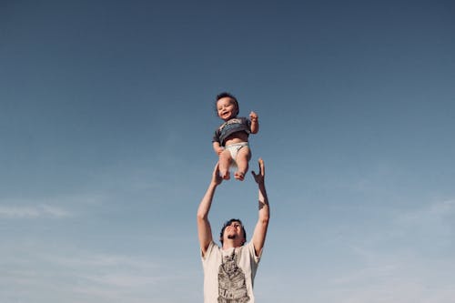 Photo of a Man Raising Baby under Blue Sky