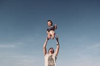 Photo of Man in Raising Baby Under Blue Sky