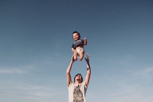 Photo of Man in Raising Baby Under Blue Sky